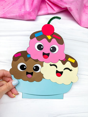 hand holding ice cream sundae paper craft on white background with pink fabric on top