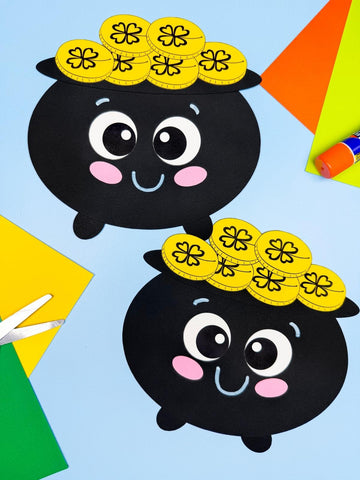 Two pot of gold shape crafts on blue background with scissors, glue stick, and papers. 