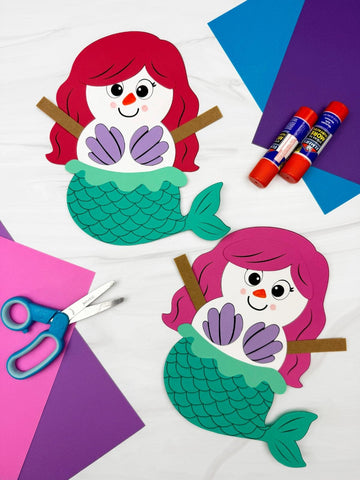 Two snowman mermaid crafts on white background with paper, scissors and glue sticks. 