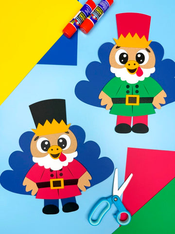 Two paper cutouts of cartoon turkeys in Nutcracker costumes with glue sticks and scissors on a colorful background.