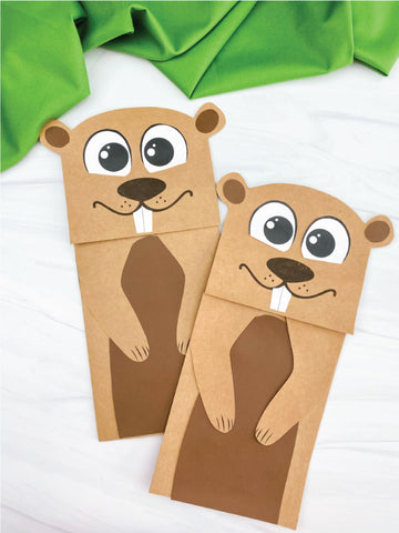 Two paper bag puppets shaped like groundhogs on a white background with green fabric.