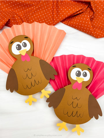 Two paper turkey cutouts on a white background with orange and pink cupcake accordion fold papers.
