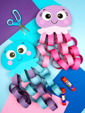 one purple and pink jellyfish, one blue and purple jellyfish. On a blue background with scissors, glue and paper. 