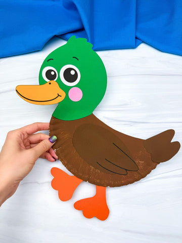 Handmade paper plate duck craft held by a person against a white background