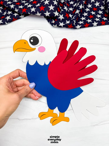 Handmade paper eagle craft held by a hand with a red, white, and blue fabric on top.