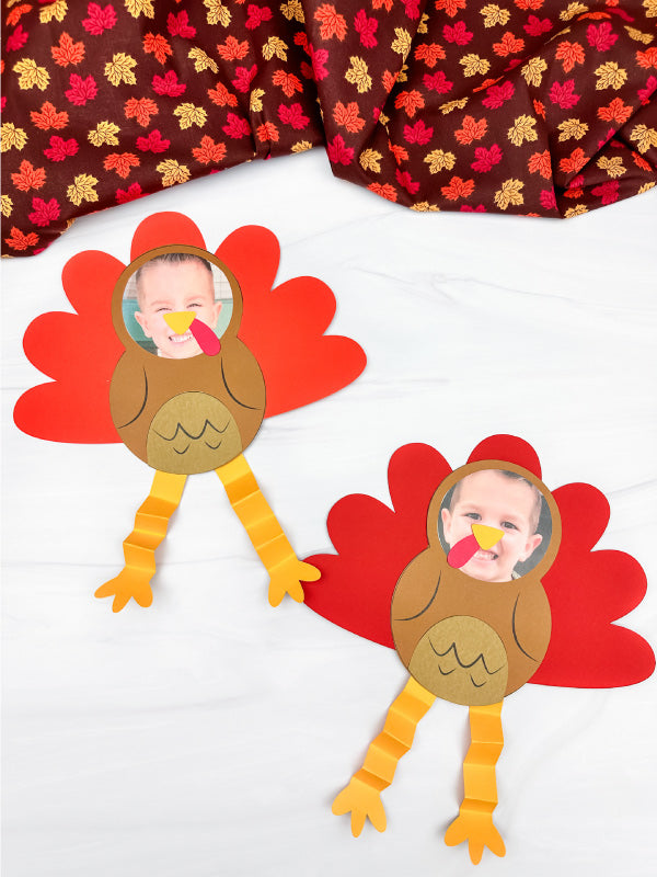 Two paper photo turkey crafts on a white background with fall leaves fabric.