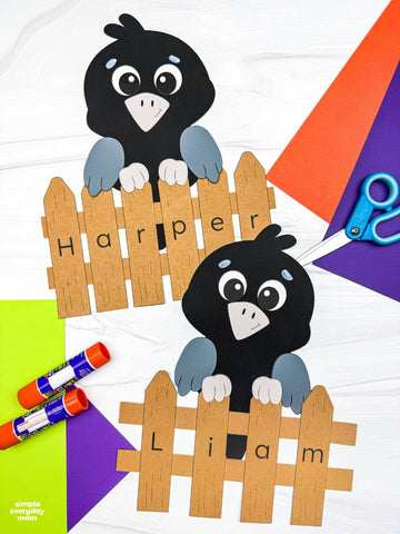 Two black bird cutouts with gray wings and letterable wooden fences are arranged on a white surface with craft supplies including scissors, markers, and colored paper. The top bird is labeled Harper and the bottom bird is labeled Liam.