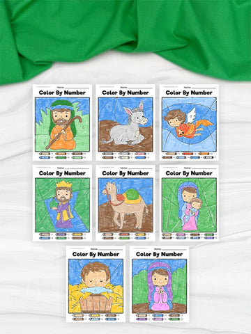 eight nativity color by number worksheets on white background with green fabric on top