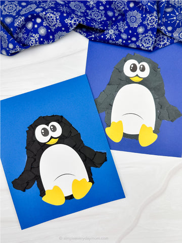 Two penguin crafts made from black, white, and yellow paper on blue cardstock with a white background and blue fabric.