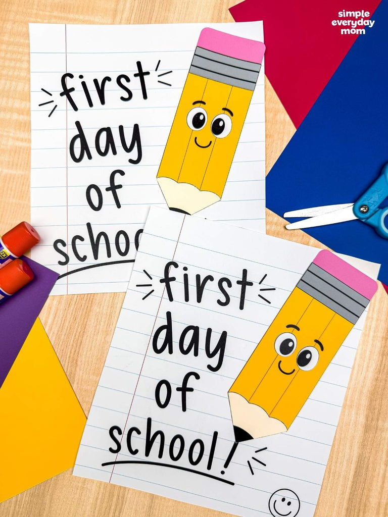 Two printable or craft paper signs reading 'first day of school' with a cartoon smiling pencil illustration, arranged on a wooden surface with craft supplies including scissors, glue, and colored paper. A 'simple everyday mom' logo appears in the top right.