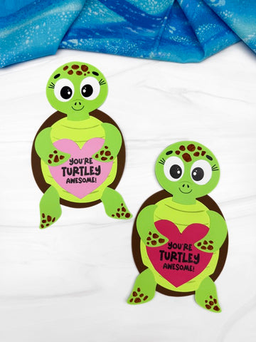 Two sea turtle valentine crafts on white background with blue fabric on top