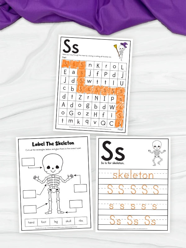 Three printable educational worksheets themed around the letter 'S' and skeleton imagery, arranged on a white fabric background with a purple cloth at the top. The worksheets include a word scramble, a skeleton labeling activity, and a tracing page with the word 'skeleton' and repeated 'S' letters.