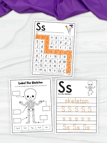Three printable educational worksheets themed around the letter 'S' and skeleton imagery, arranged on a white fabric background with a purple cloth at the top. The worksheets include a word scramble, a skeleton labeling activity, and a tracing page with the word 'skeleton' and repeated 'S' letters.
