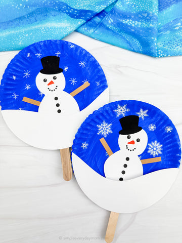 Two paper plate snowmen on sticks with blue backgrounds and snowflake decorations.