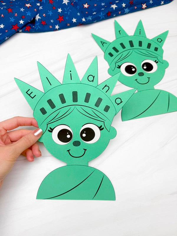 hand holding Statue of Liberty name craft on white background with patriotic fabric on top