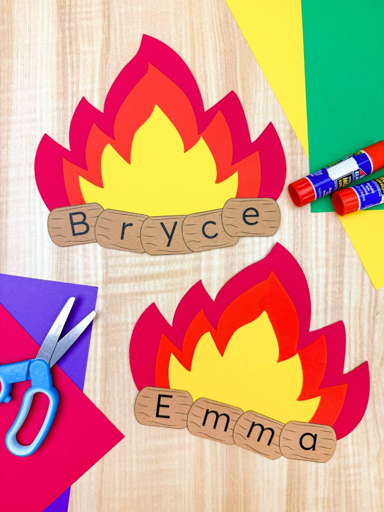 Two campfire name crafts on wooden background with colorful paper, scissors and glue 