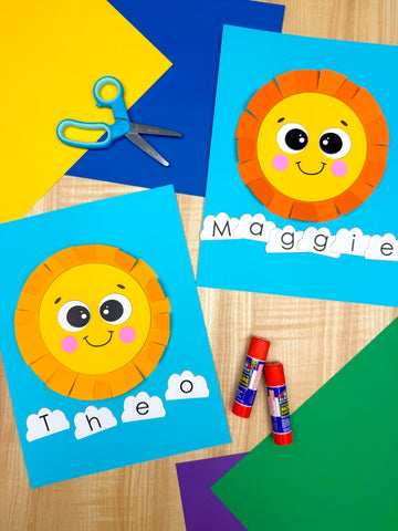 Children's craft project with sun and letter cloud cutouts, scissors, and glue sticks on a wooden surface.