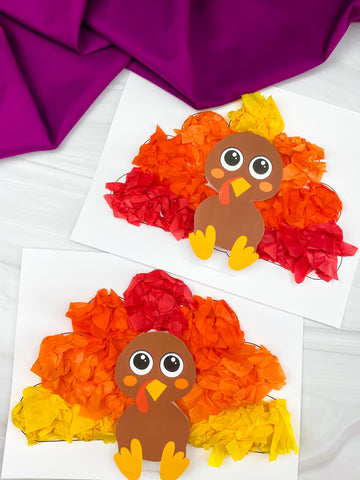 Two colorful paper turkeys on white paper with a purple fabric background
