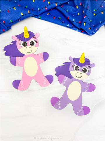 Two colorful paper unicorn gingerbread disguise crafts on a white background with a blue fabric and lights in the background.