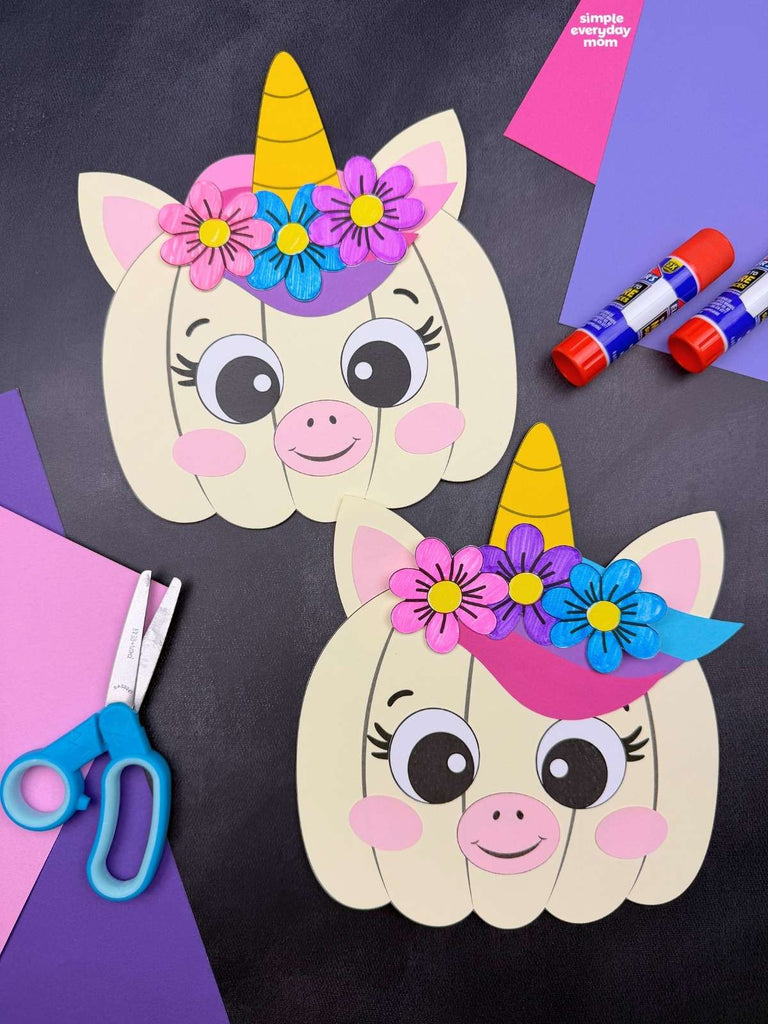 Two unicorn pumpkin disguise crafts on black background with paper, scissors, and glue. 