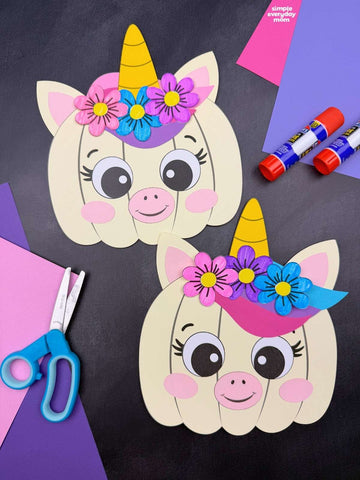 Two unicorn pumpkin disguise crafts on black background with paper, scissors, and glue. 