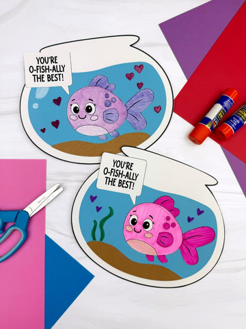 Two Valentine fish bowl crafts on white background with colorful paper, scissors, and glue sticks. 