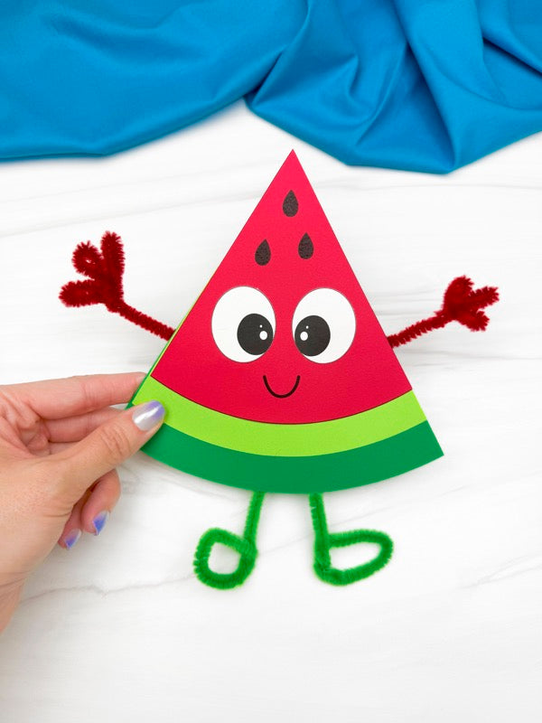 hand holding watermelon craft on white background with blue fabric on top
