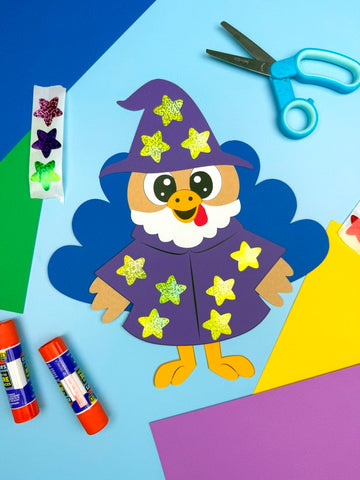 Paper turkey disguised as a wizard on a colorful background with scissors, stickers, and glue sticks